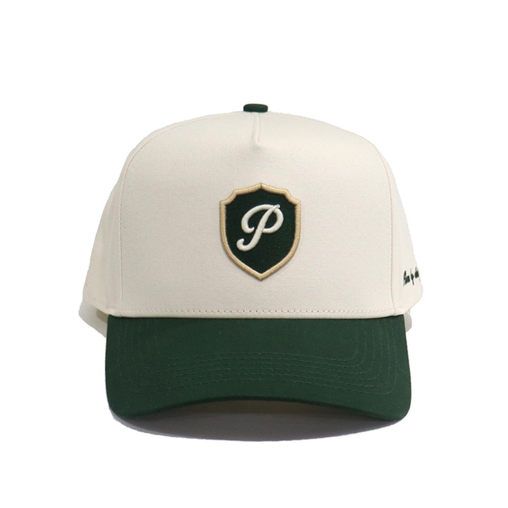 The Club Cap by Purist Golf — cream crown with a deep-green brim and embroidered crest